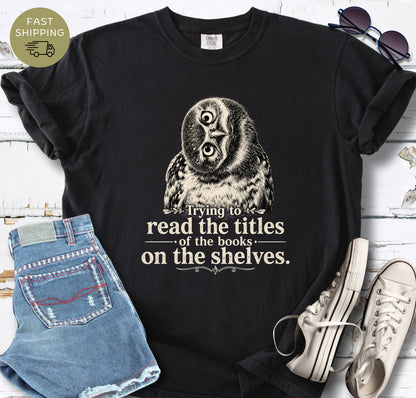 Comfort Colors reading shirt with a curious owl graphic and text about reading book titles on shelves.