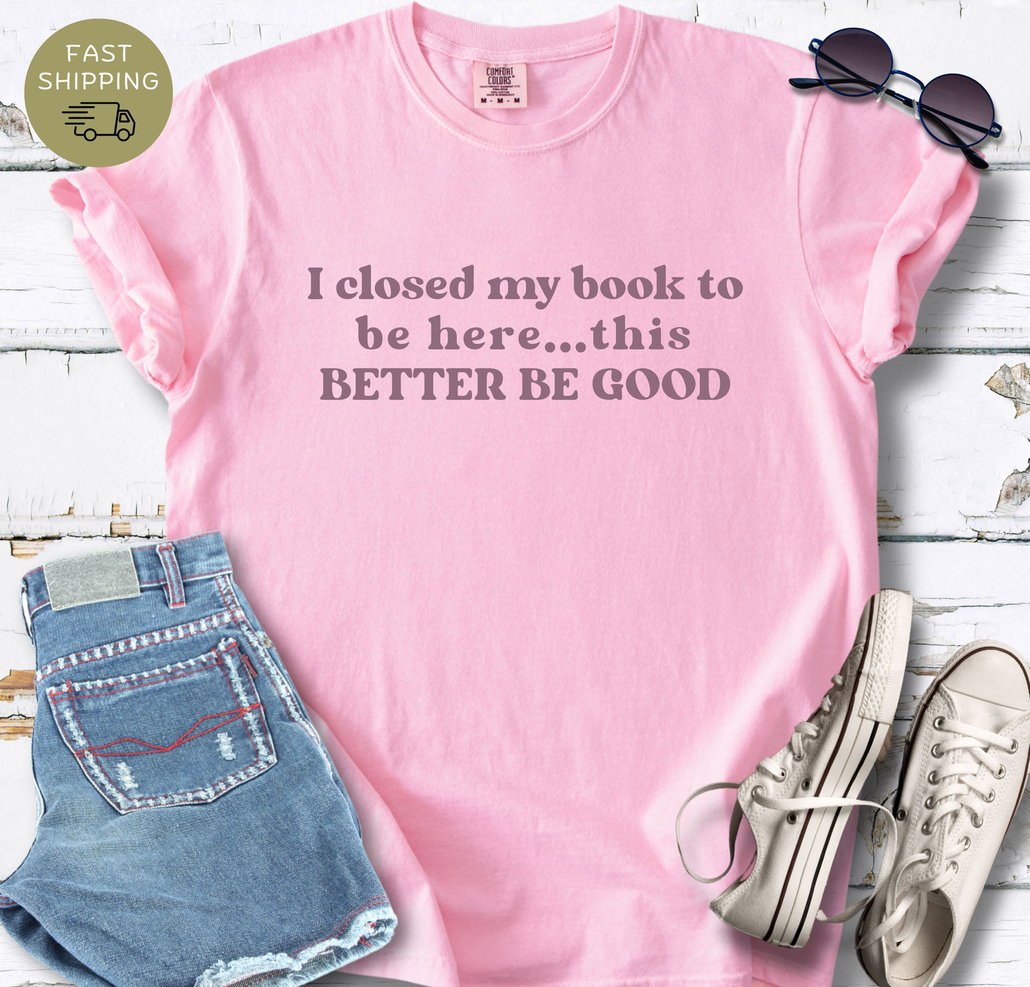 Close-up view of the "I closed my book to be here" slogan printed on a high-quality Blossom cotton t-shirt. The text is centered and rendered in a bold, retro serif typography.