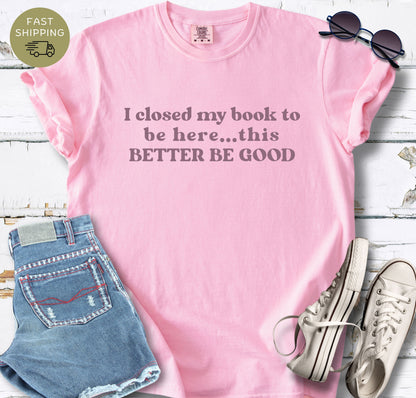Close-up view of the "I closed my book to be here" slogan printed on a high-quality Blossom cotton t-shirt. The text is centered and rendered in a bold, retro serif typography.