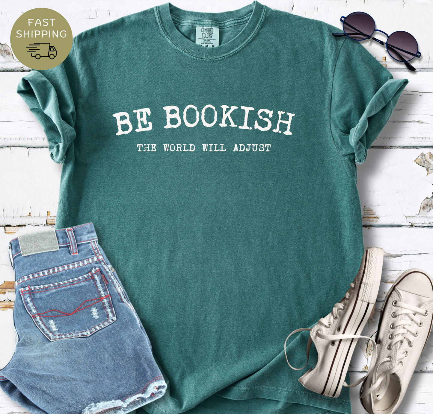 Be Bookish graphic tee styled in a flat lay with denim shorts, sneakers, and sunglasses.