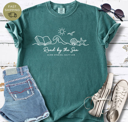 Beach reading t-shirt with shells, wave, and “Read by the Sea” text
