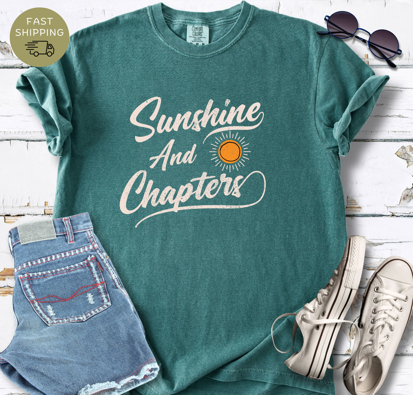 A blue spruce  Comfort Colors t-shirt featuring the text "Sunshine And Chapters" in a vintage cream script with a small orange sun graphic.