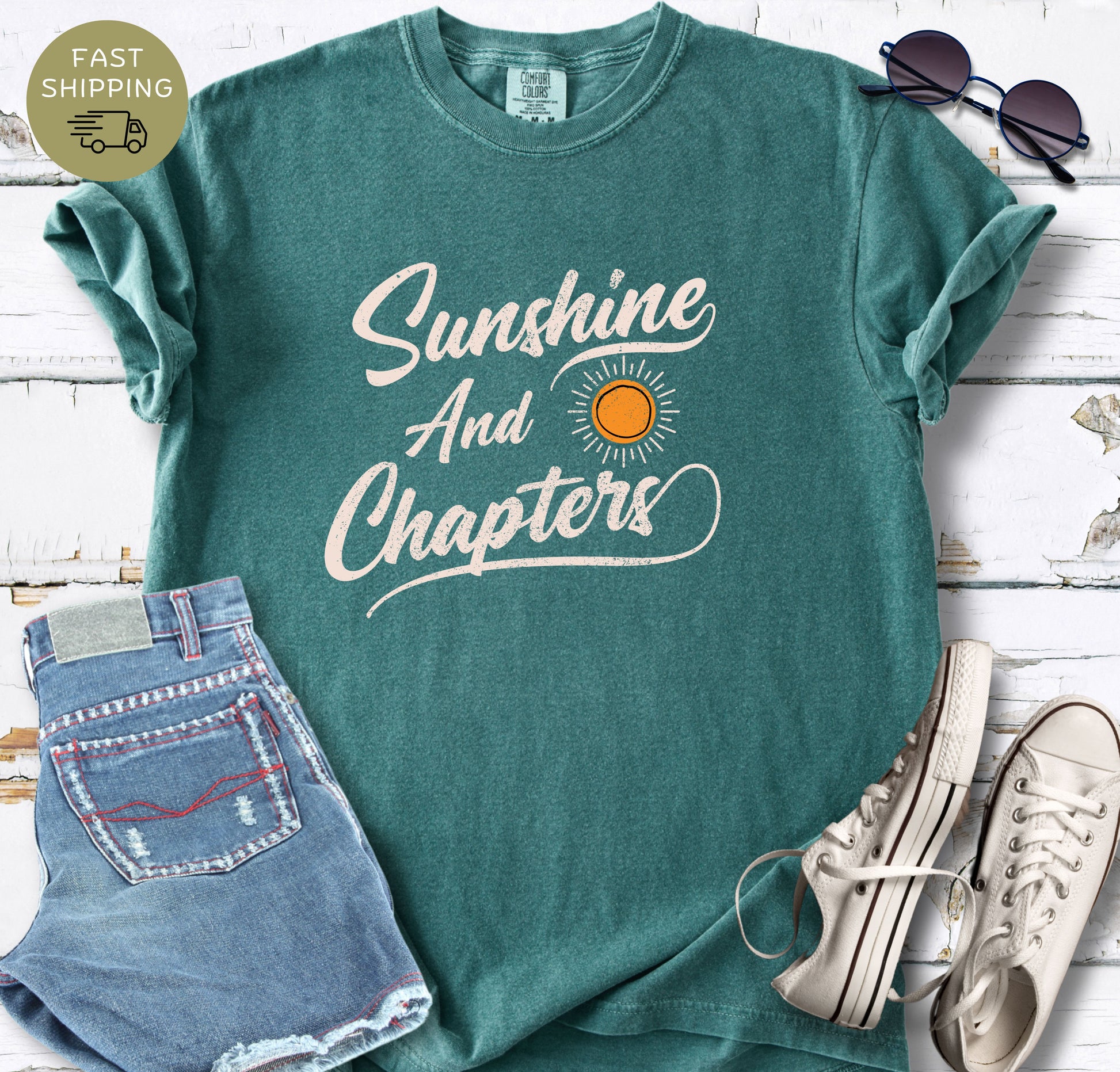 A blue spruce  Comfort Colors t-shirt featuring the text "Sunshine And Chapters" in a vintage cream script with a small orange sun graphic.