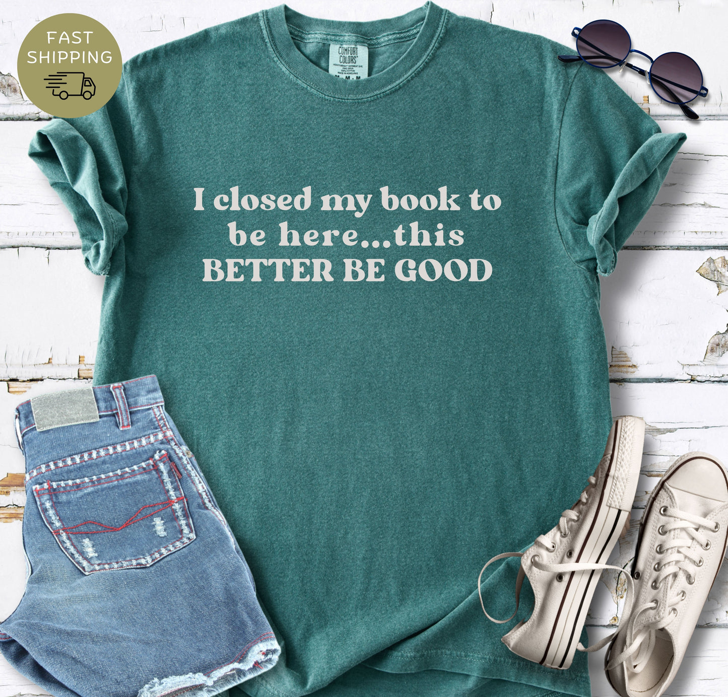Front view of a Blue Spruce short-sleeve crewneck tee. The shirt features a funny reading quote: "I closed my book to be here... this BETTER BE GOOD" in a soft, screen-printed off-white ink.