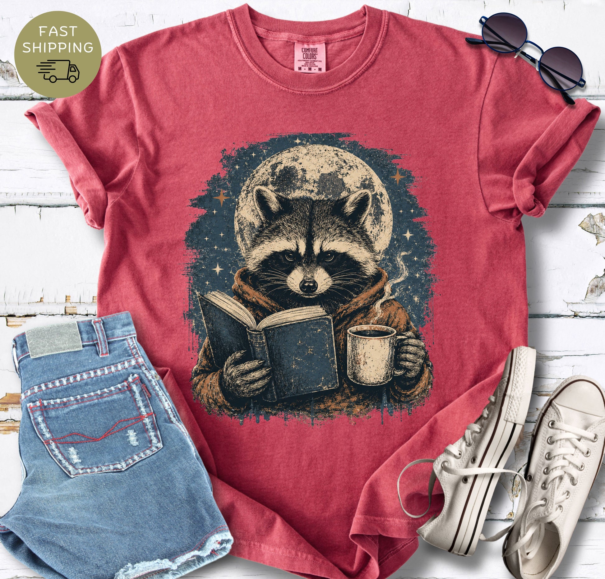 Vintage-style book lover shirt with woodland raccoon, open book, and warm mug.