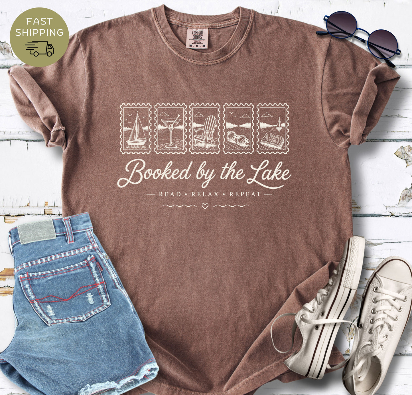 Summer reading T-shirt with sailboat, beach chair, sunglasses and open book illustrations.