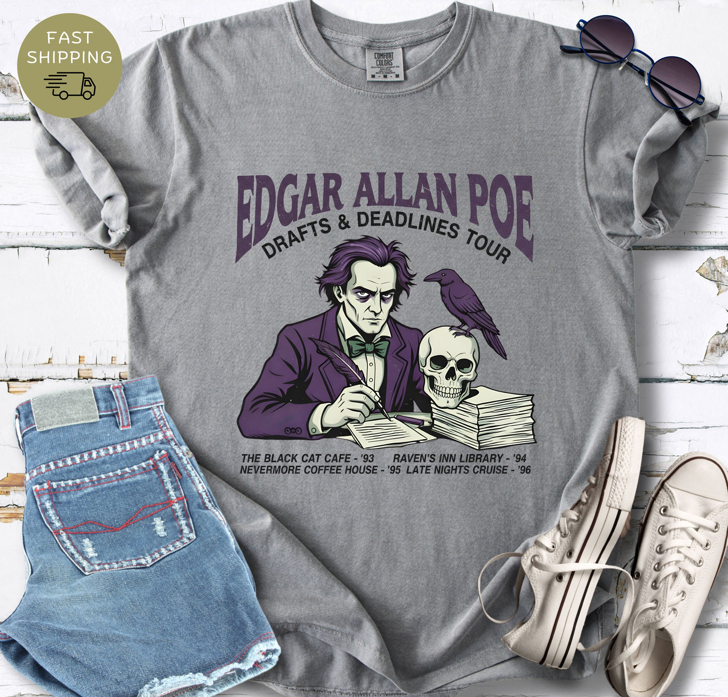 Gray t-shirt with Illustrated Edgar Allan Poe wearing a purple suit, writing at a desk with a raven and skull, styled like a vintage literary tour t-shirt design.