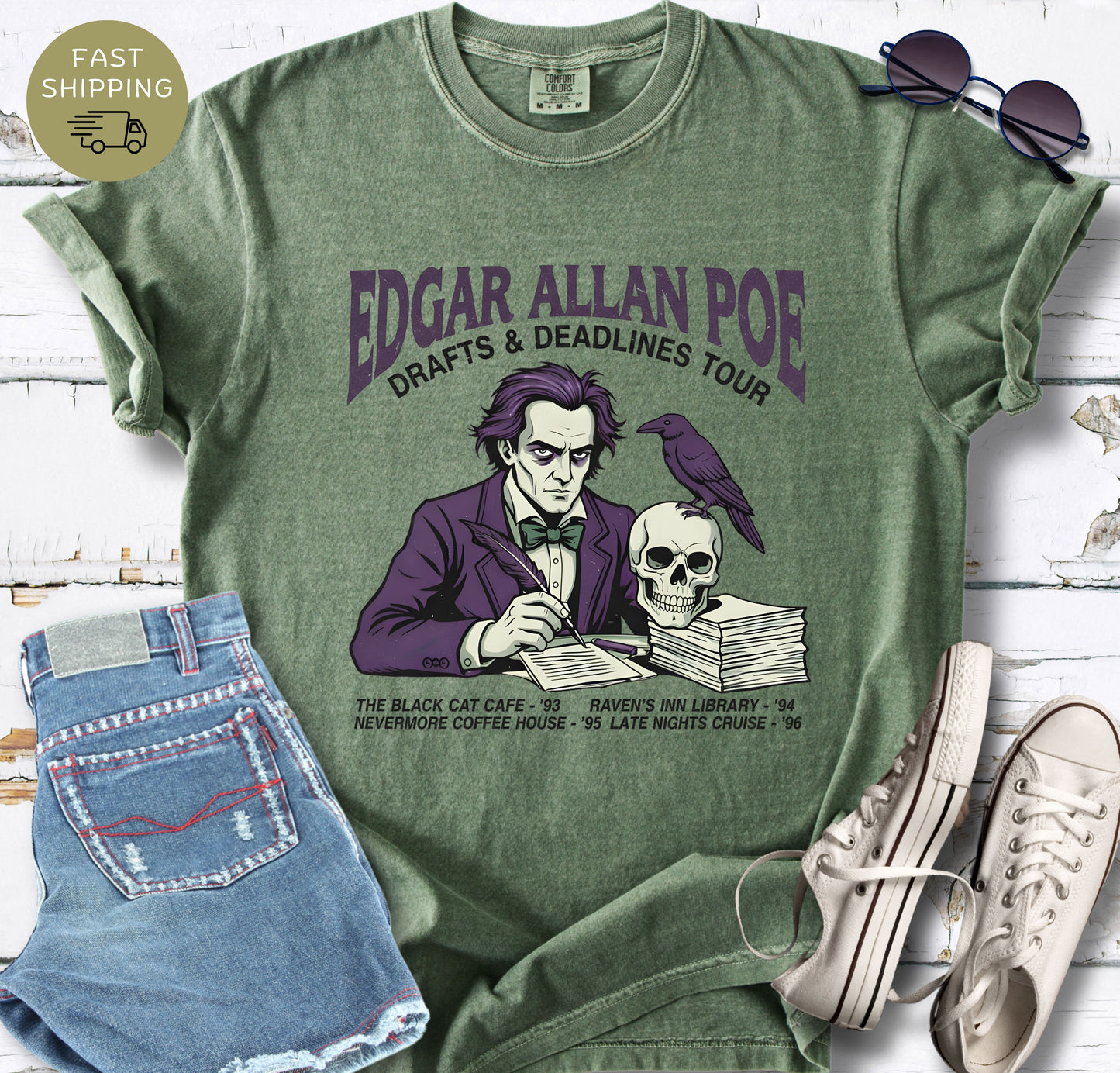 Illustrated Edgar Allan Poe wearing a purple suit, writing at a desk with a raven and skull, styled like a vintage literary tour t-shirt design.